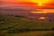 Sun setting over a field of eolian wind turbines and a valley wi