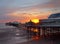 The sun setting over the historic north pier in blackpool with glowing light reflected on the beach and colourful twilight sky