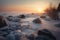 the sun is setting over the water and rocks covered in ice and snow on a frozen lake shore with trees and bushes in the