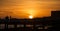 Sun setting silhouette on shore over pier and walkway