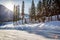 Sun shines from behind a mountain next to trees behind a hard snow packed road