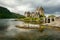 Sun shines through clouds on Eilean Donan castle with rocks in f