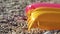 Sun shines to yellow and pink coloured inflatable with drops on water at surface, small pebbles beach under, closeup detail,