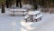 Sun shining on picnic benches and table covered with thick layer of snow in forest