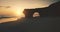 Sun silhouette of rock wall with giant hole on sand beach aerial view. Seascape of ocean cliff coast