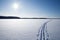 Sun, snow and Ski track crossing a frozen lake