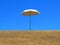 Sun umbrella on dry lawn against blue sky