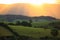 Sunbeams over green hills landscape by golden sky in Australia