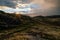 Sunburst over trail in the mountains with dramtic rain heavy clouds and blue skies to the left.