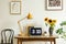 Sunflowers, yellow lamp and laptop on wooden desk in home office interior with posters. Real photo