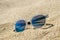 Sunglasses on the beach. Multi colored stylish model with transparent frame and blue lenses. Vacation concept.