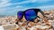 Sunglasses with blue lenses lie on a sandy shell beach on the sea front in sunny weather. Recreation and tourism concept