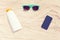 sunglasses, frameless smartphone, sunscreen bottle on a white sand
