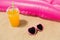 Sunglasses, juice and pool mattress on beach sand
