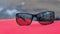 Sunglasses on red plaid on bonfire background in forest camping, closeup.