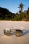 Sunglasses on sandy beach over tropical island background