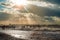 Sunlight breaks through the clouds and illuminating a pier and stormy beach