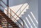 Sunlight and shadow on surface of the old metal staircase on gray sandwich panel wall outside of cold storage room