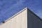 Sunlight on surface of white corrugated steel warehouse wall  against clouds on blue sky