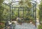 A sunlit conservatory with wrought iron furniture, lush potted plants, and a mosaic-tiled floor,