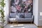 Sunlit, gray sofa by a floral print wall in the nook of a feminine living room interior with golden accessories