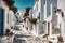 sunlit narrow traditional greek town street with ancient white houses in summer sunlight