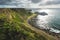 Sunlit ocean, green shore with road. Ireland.