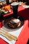 Sunlit outdoor table setting with a savory dish on a glittery plate, red tablecloth, sliced vegetables, black cup, and golden