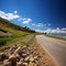 Sunlit road ascends towards hill, under a summers blue sky