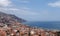 Sunlit view of the city of funchal from above with rooftops and buildings in front of a bright blue sea