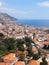 sunlit view of the city of funchal from above with rooftops and buildings in front of a bright blue sea