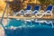 Sunloungers near swimming pool and reflected their in blue water