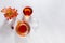 Sunny autumn teatime with rose hip tea with teapot, cup, orange rose hip branch with shadows on white wood table top view.