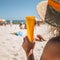 Sunny beach and sand for National Sunscreen Day. Woman in hat hold cream tube under sun on summer vacation. Generative AI