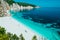 Sunny Fteri beach lagoon with rocky coastline, Kefalonia, Greece. Tourists under umbrella chill relax near clear blue