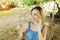 Sunny light portrait of young blonde girl talking by smartphone and riding swing in Bali, sand in background.