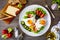 Sunny side up eggs on toasted bread and prosciutto with fresh green vegetables, mini tomatoes and black olives on wooden table