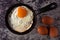 Sunny side up fried egg in cast iron skillet with whole eggs on concrete background. Top view