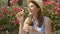 Sunny summer day. Young funny girl blowing air soap bubbles. Beautiful pink flowers on background