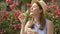 Sunny summer day. Young funny girl blowing air soap bubbles. Beautiful pink flowers on background