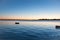 Sunrise across bay with small dinghy blue tones with orange around horizon