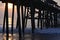 The sunrise appears through the beach pier pilings and reflects on the ocean waves