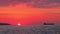 Sunrise with burning red sky over sea waves and industrial cargo ship