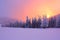 Sunrise enlightens sky, mountain and trees standing in snowdrifts covered by frozen snow with yellow shine.