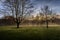 Sunrise in foggy park shining with sun rays through the trees and branches. Beautiful scenic view on a silent and tranquil morning