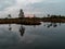 Sunrise landscape with peat bogs and swamp vegetation. The bog pond reflects small pines, bushes and cloudy skies