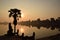 Sunrise over beautiful lake in angkor wat with sun reflecting in the water and palm in foreground, focus