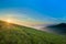 Sunrise over hills in mountains with green grass and blue sky wi