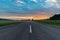 Sunrise over a straight road through green fields