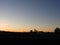 Sunrise peaks from behind a hill with pole barn silhouette